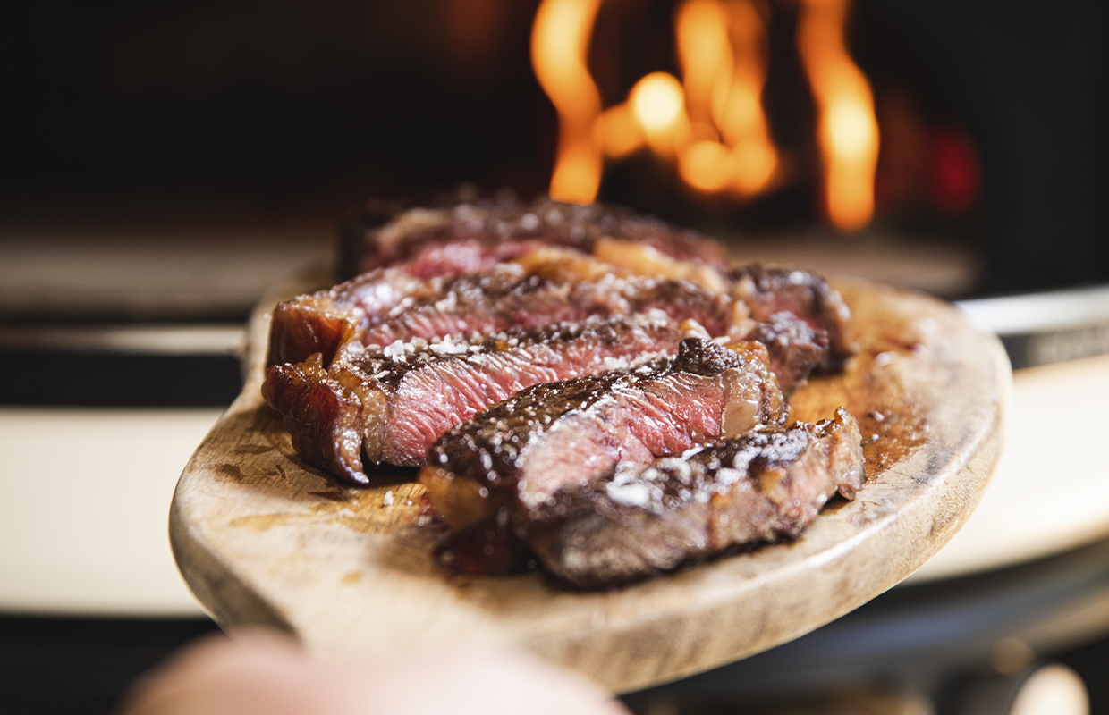 Steak cut up on board in front of pizza oven